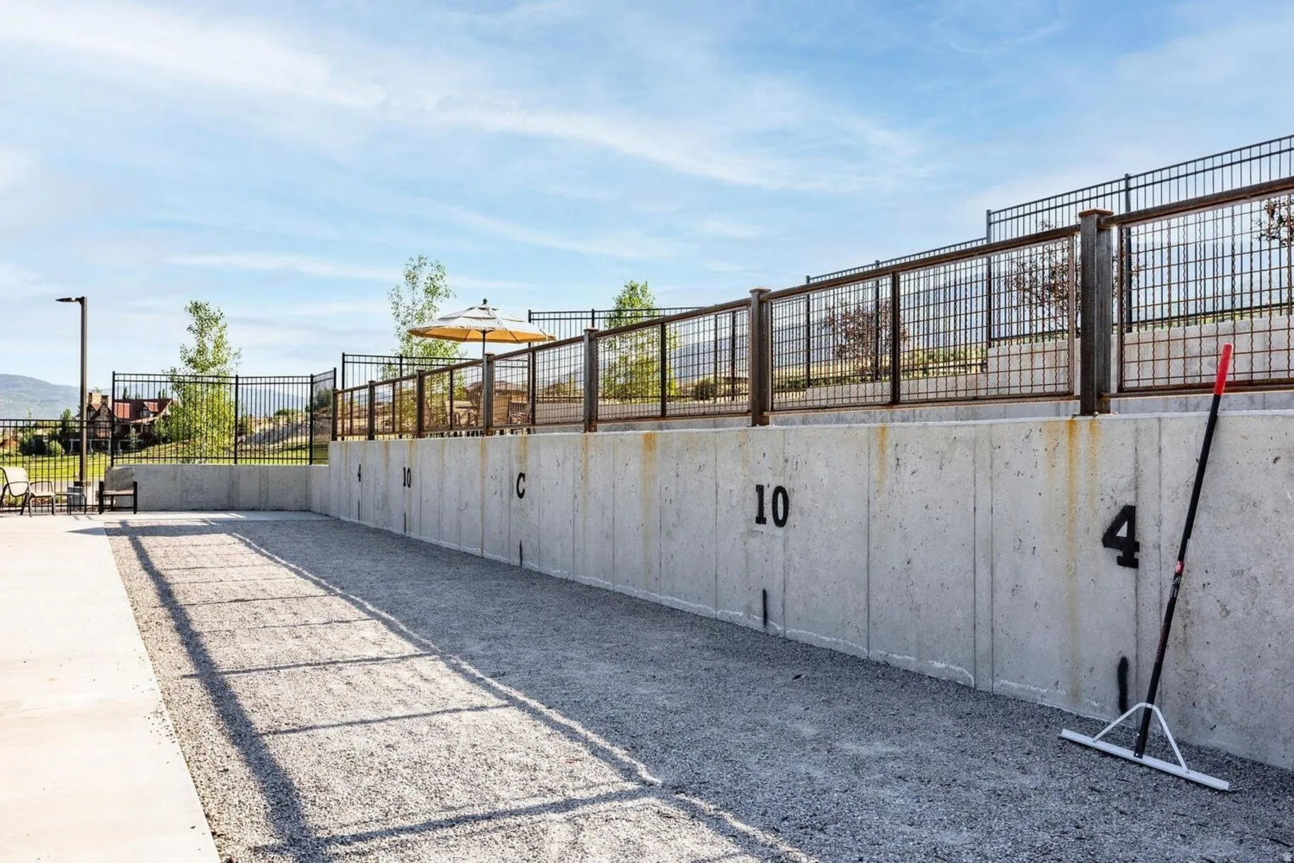 Outdoor bocce court with concrete retaining wall, metal grid fencing, and adjacent paved area