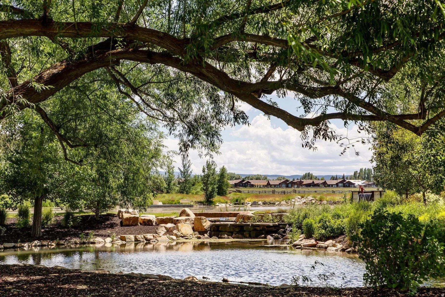 Manicured pond featuring natural rock landscaping and a pedestrian bridge, framed by mature trees