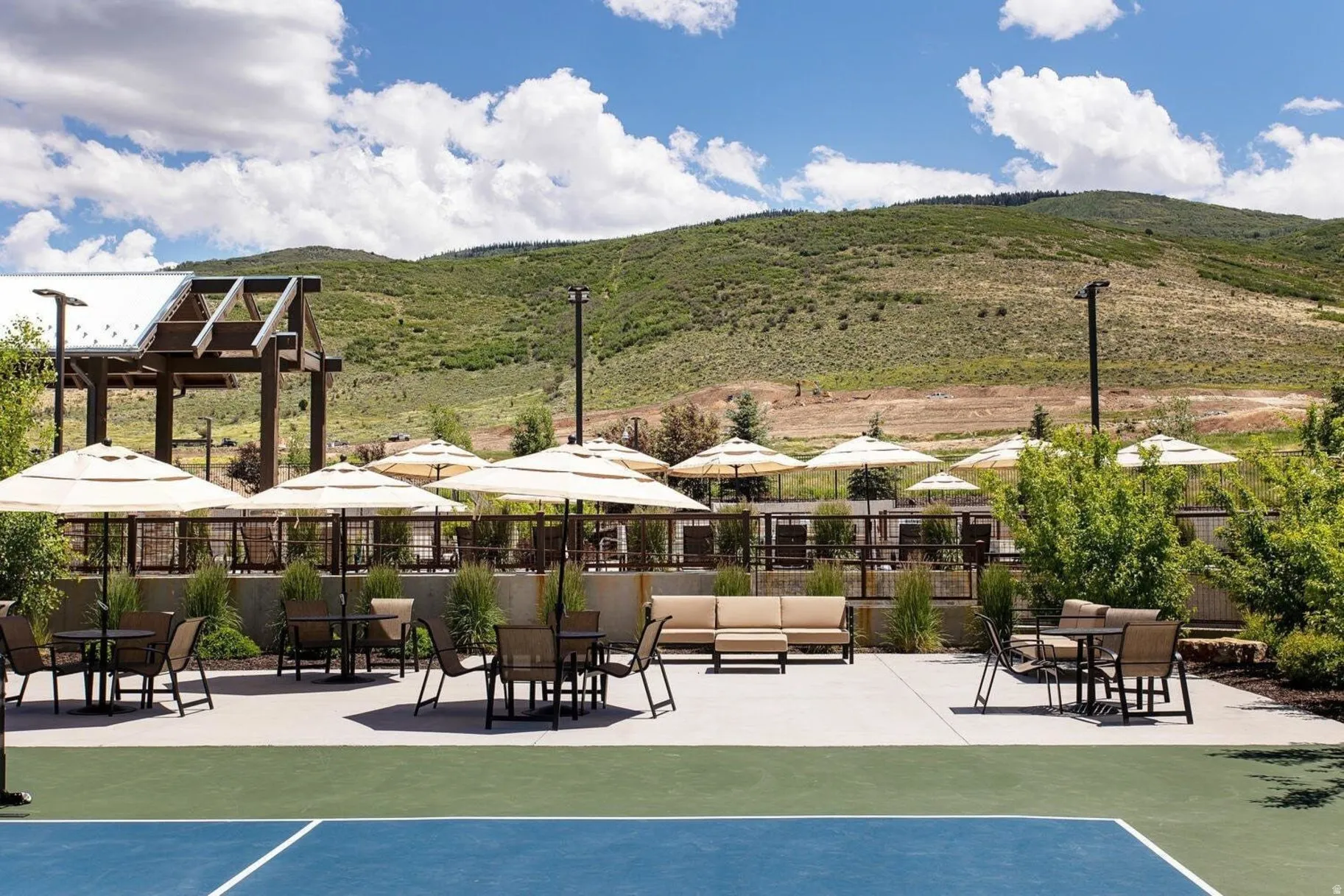 Outdoor patio area featuring multiple seating arrangements with umbrellas, a paved surface, and a backdrop of rolling hills