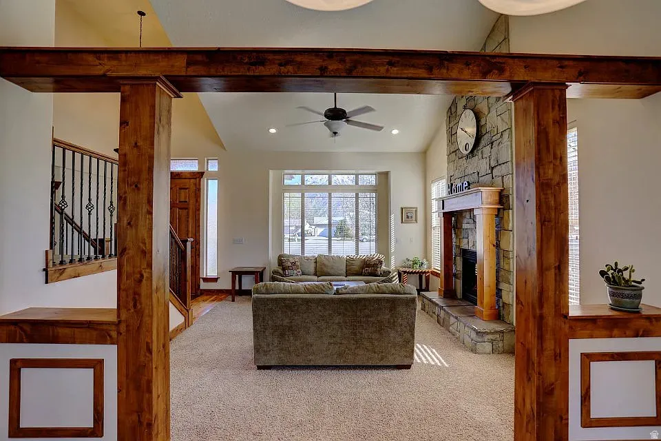 Spacious living area featuring a vaulted ceiling and a stone-faced fireplace with a wood mantle