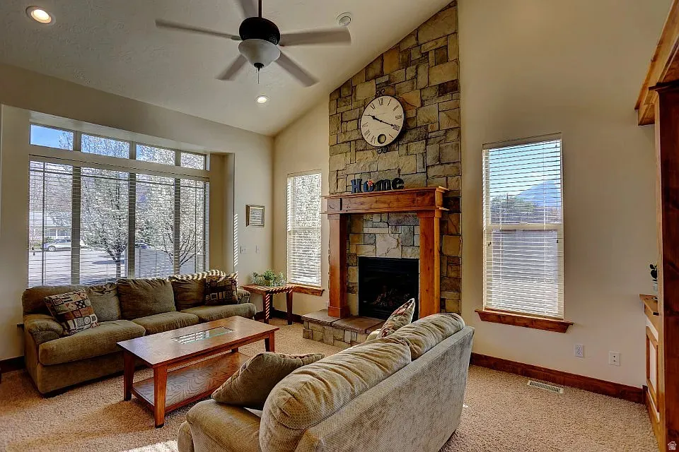 Spacious living area featuring a vaulted ceiling with a ceiling fan, stone-faced fireplace with a wood mantel, expansive bay window, and recessed lighting