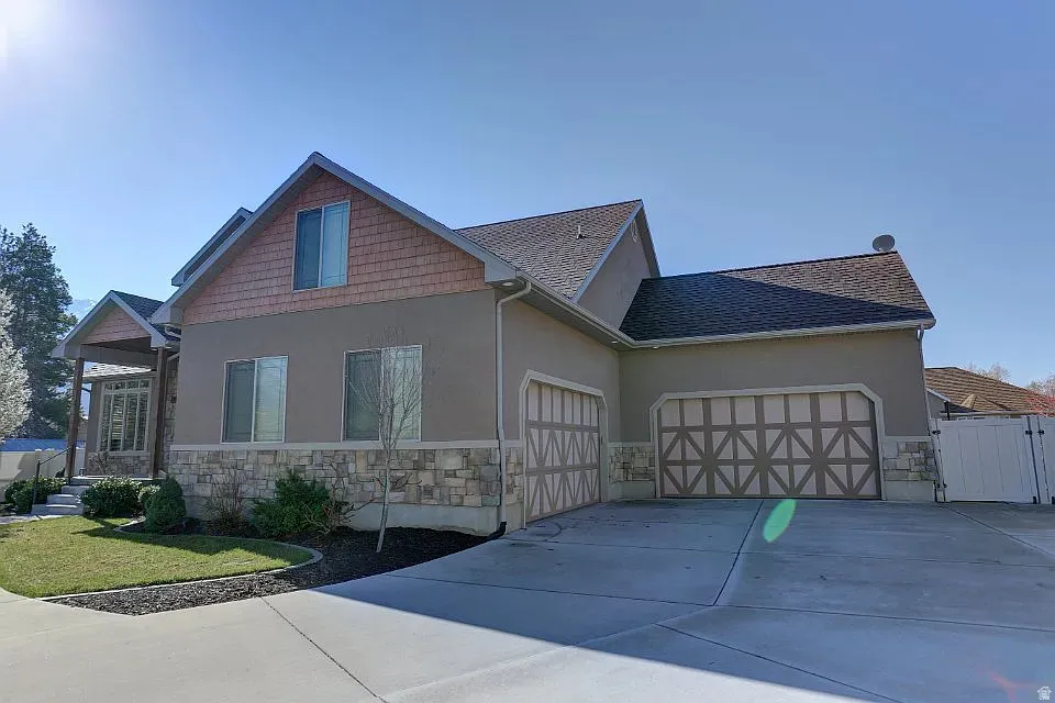 Stucco and stone exterior featuring a covered entry, multiple windows, and a multi-car garage with decorative doors
