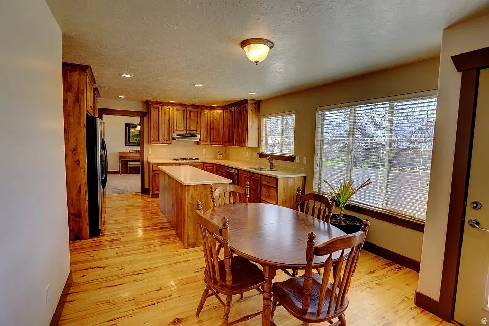 Kitchen featuring wood-finish flooring, natural wood cabinetry, light-toned countertops, a central island, and multiple windows