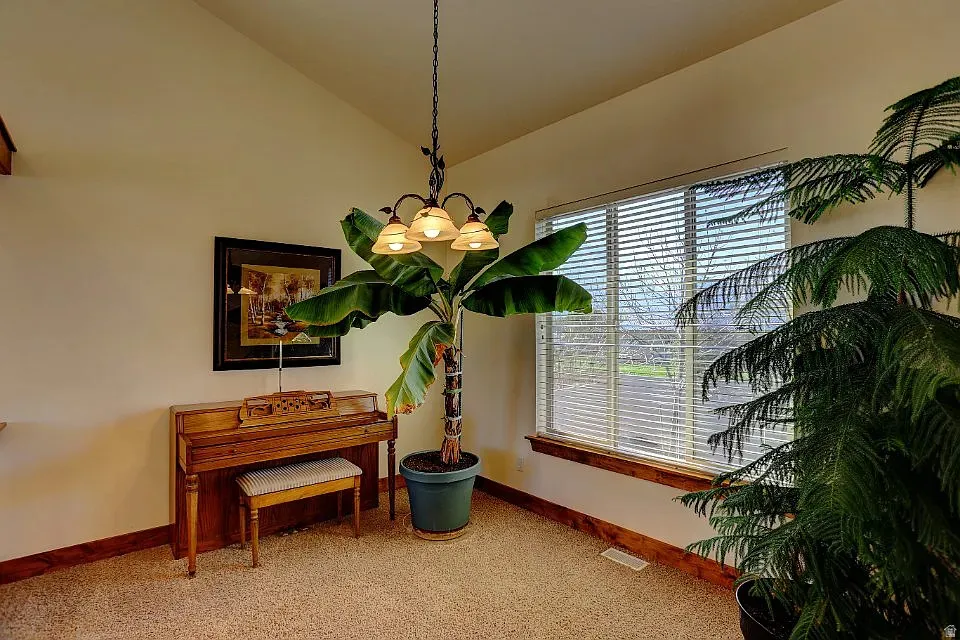Vaulted ceiling room featuring a large window with horizontal blinds, natural wood trim, wall-to-wall carpeting, and an overhead chandelier with three frosted glass shades