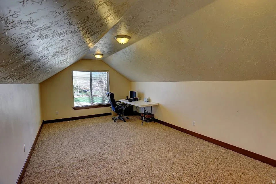 Carpeted attic space with sloped ceilings and a window overlooking exterior landscaping