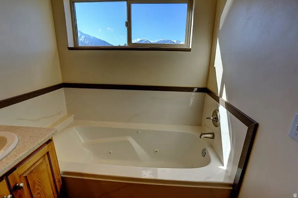 Soaking tub with integrated jets, surrounded by white stone-look paneling and a dark accent trim