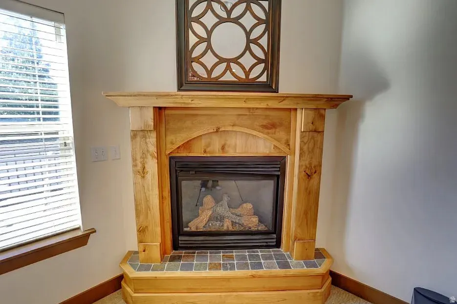 Corner fireplace featuring a natural wood mantel and hearth, gas insert, and multi-tone tile surround