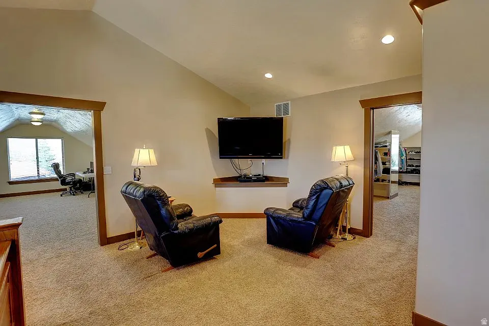 Carpeted living area featuring a vaulted ceiling with recessed lighting, wood-trimmed doorways, and a built-in wall niche with a wood shelf