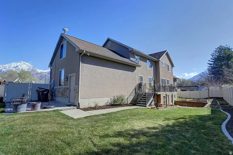 Rear exterior featuring a spacious lawn, multi-level deck, and stone accents