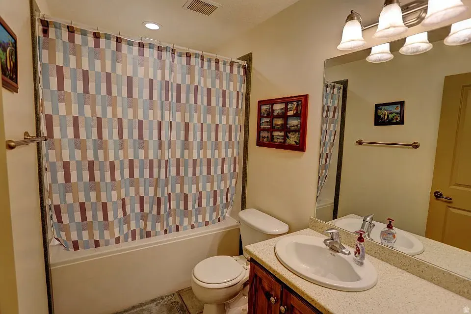 Bathroom featuring a built-in bathtub with shower, a vanity with a white oval sink and chrome faucet, a stone-look countertop, and a wood-finish vanity cabinet