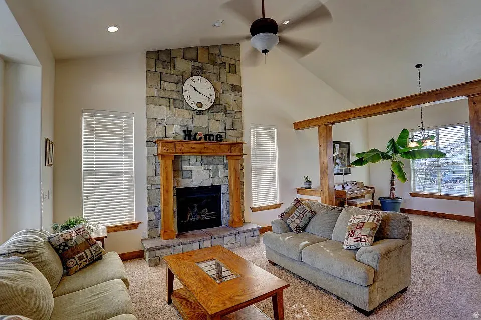Living area featuring a stone-clad fireplace with a wood mantel, vaulted ceiling, and exposed wood beam accents