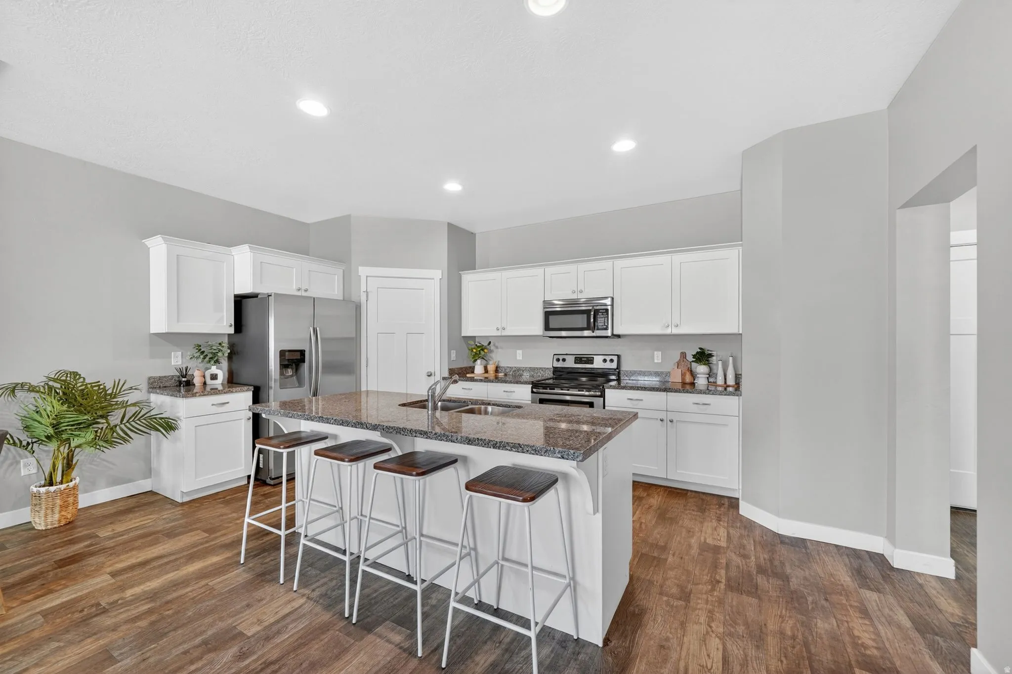 Open-concept kitchen featuring an oversized island with seating, white shaker-style cabinetry, stainless steel appliances, and wood-finish flooring