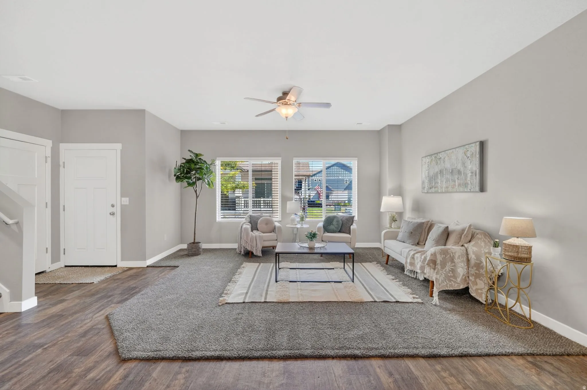 Spacious living area featuring wood-finish flooring, a ceiling fan, and two windows with horizontal blinds