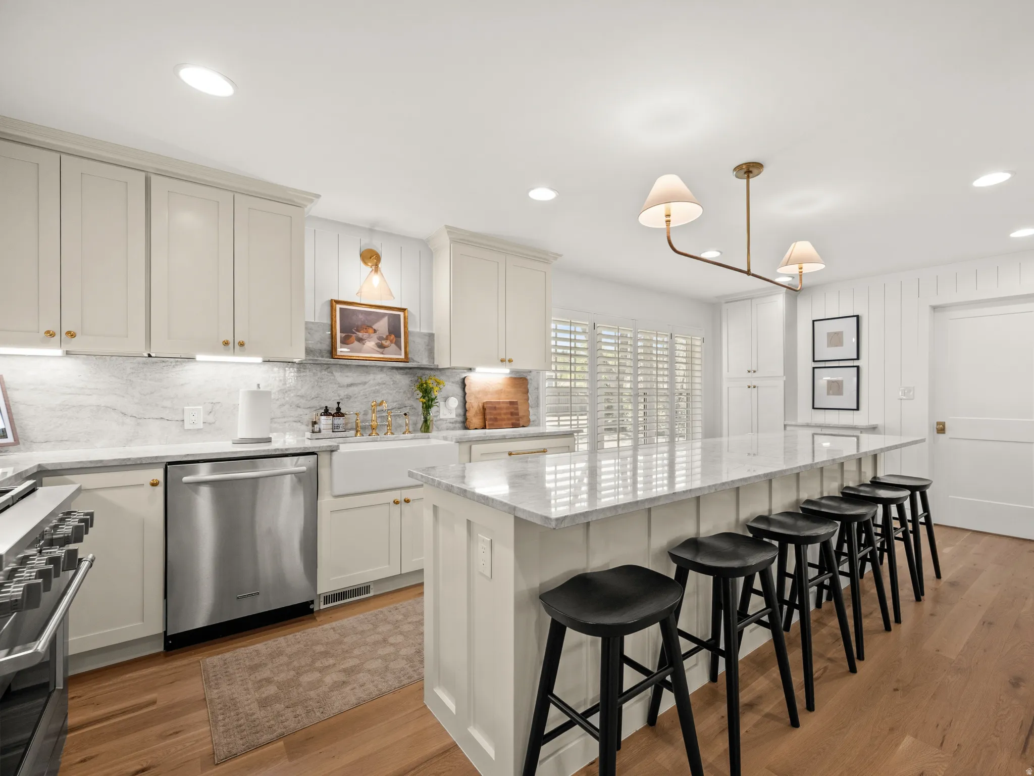 Expansive kitchen featuring a large central island with seating for six, light-toned cabinetry, stainless steel appliances, a farmhouse sink, and wood-finish flooring