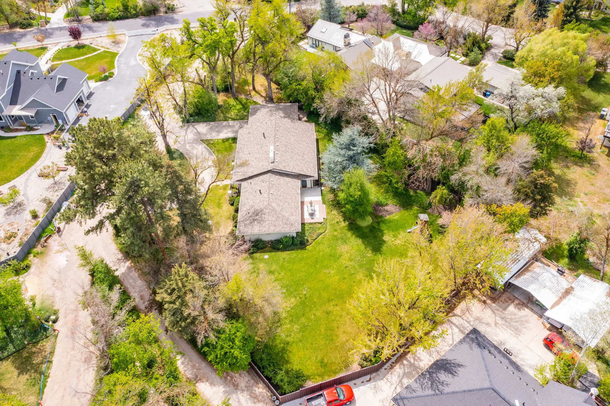 Expansive property featuring a prominent residence, lush green lawn, mature trees, a private driveway, and surrounding residential properties