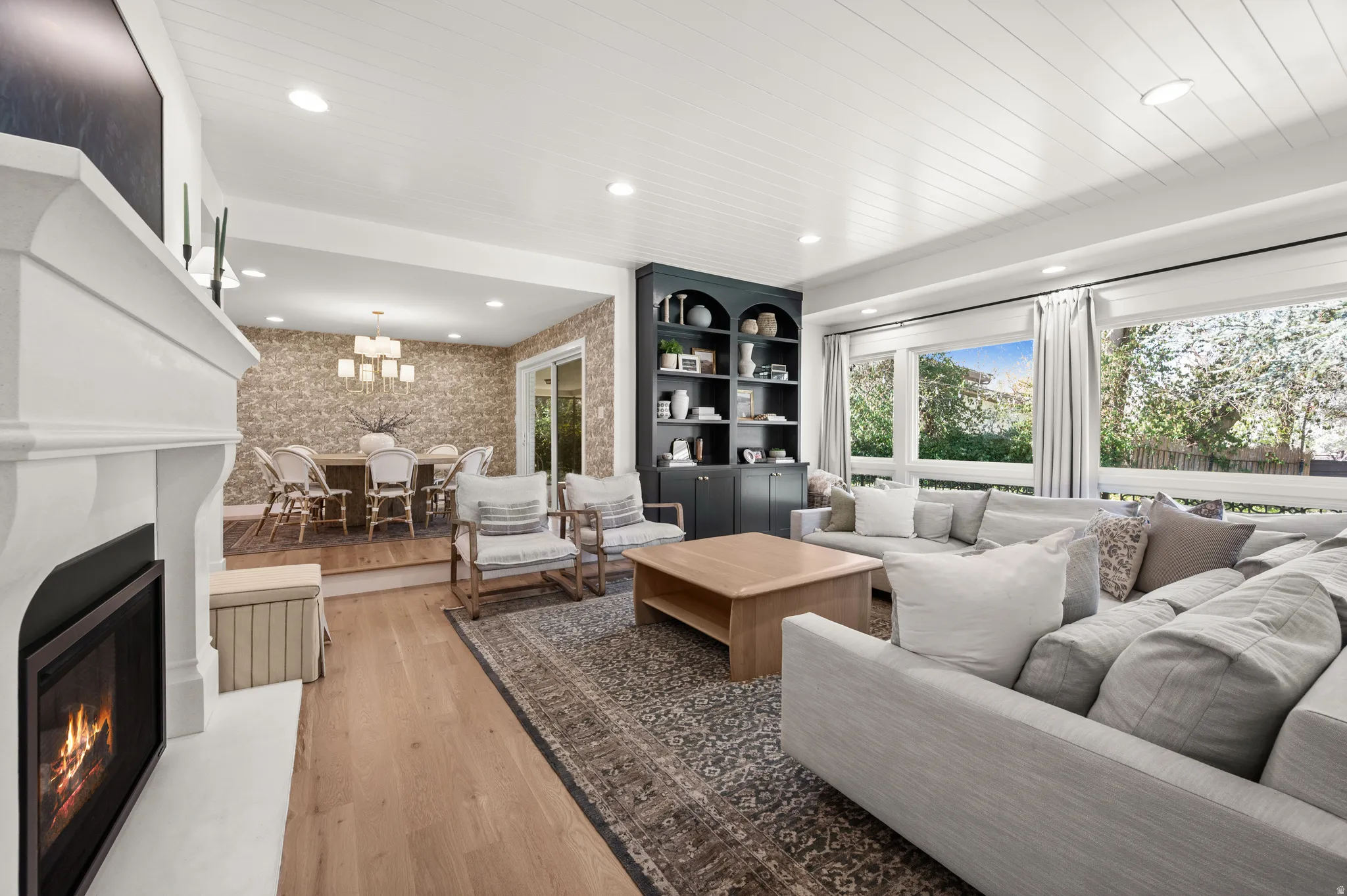 Spacious living room featuring wood-finish flooring, a white mantel fireplace, built-in shelving, and large windows