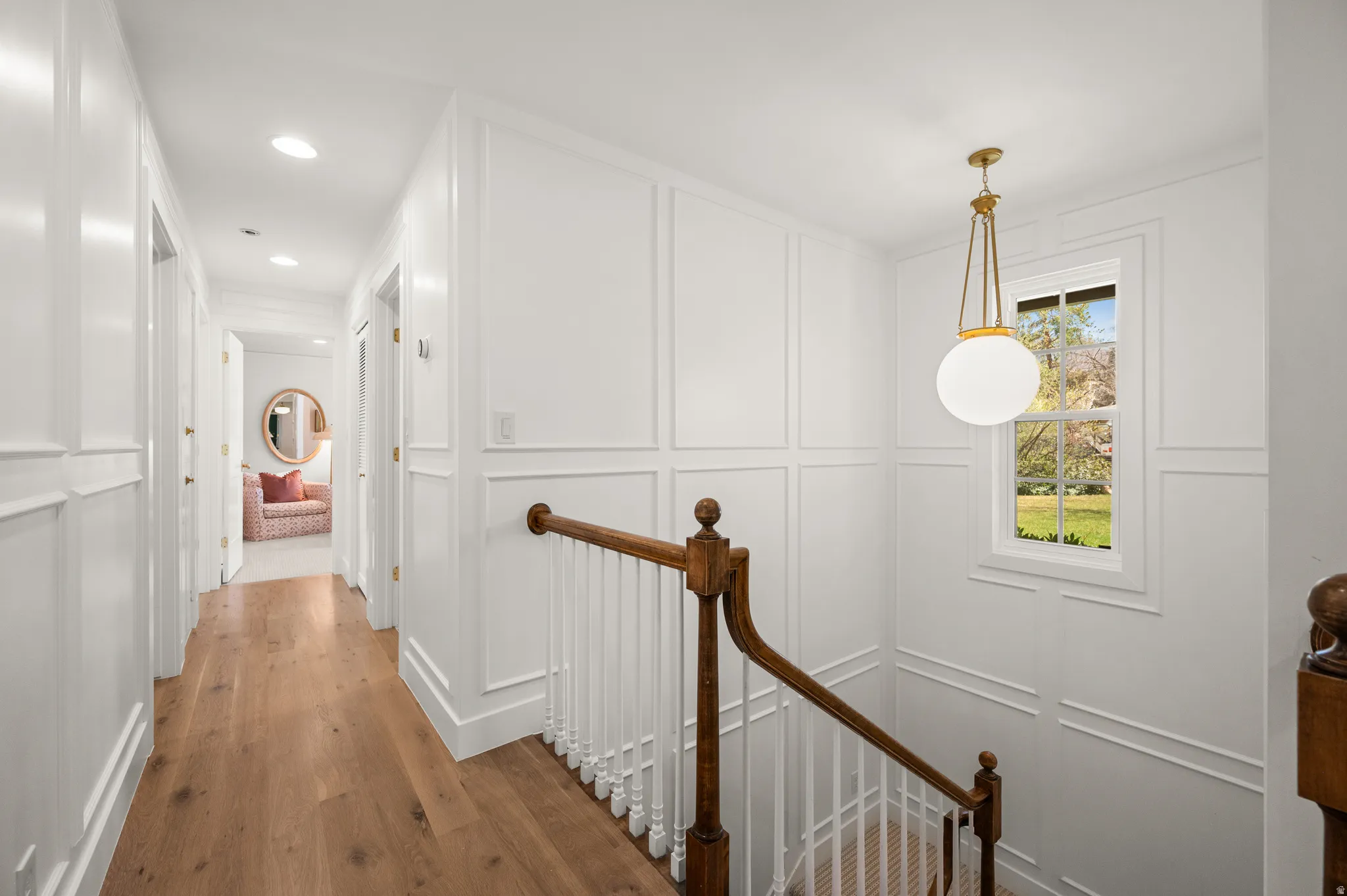 Hardwood flooring throughout a hallway featuring recessed lighting and wainscoting