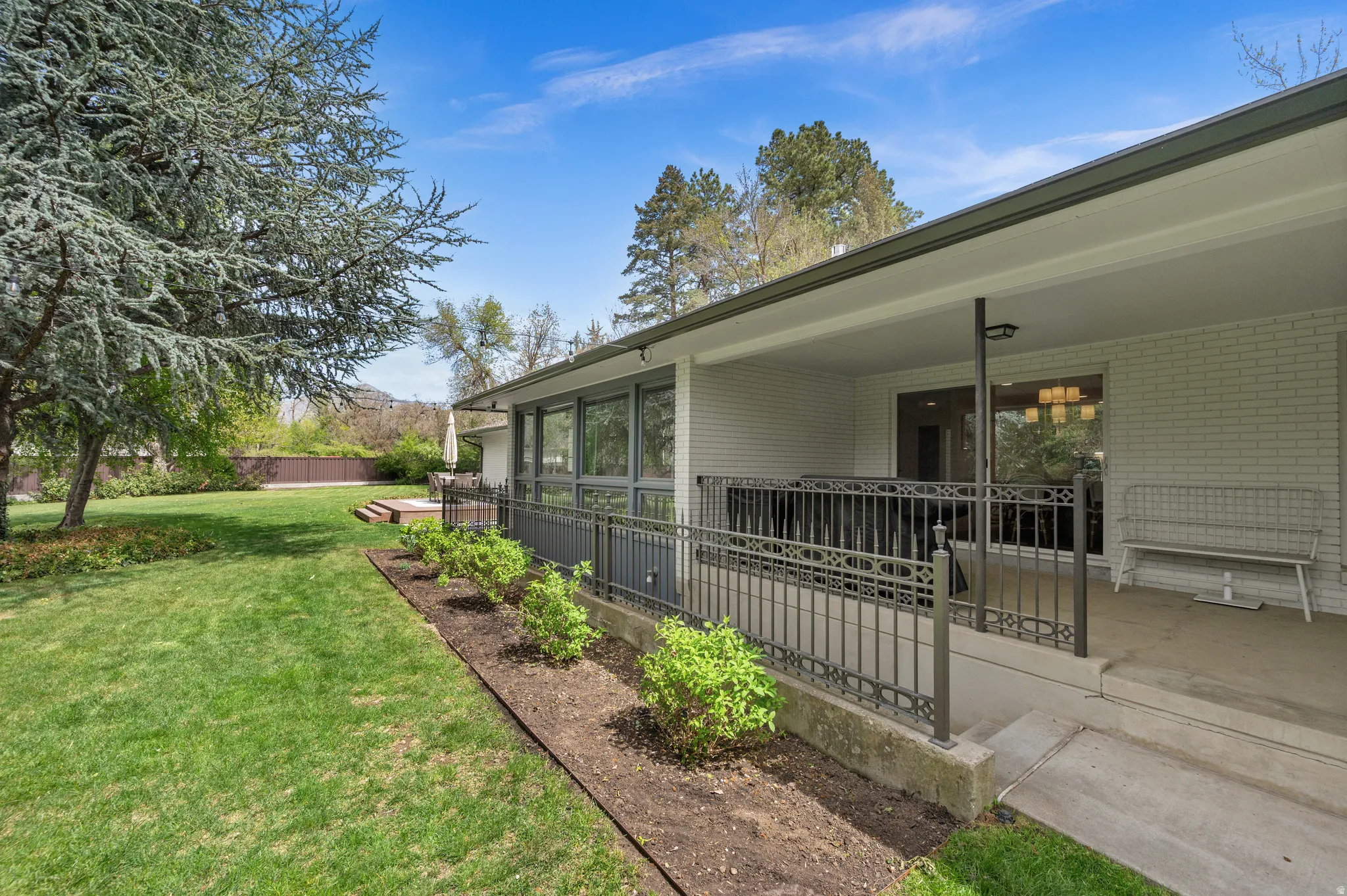 Spacious backyard featuring a manicured lawn, mature trees, and a covered patio