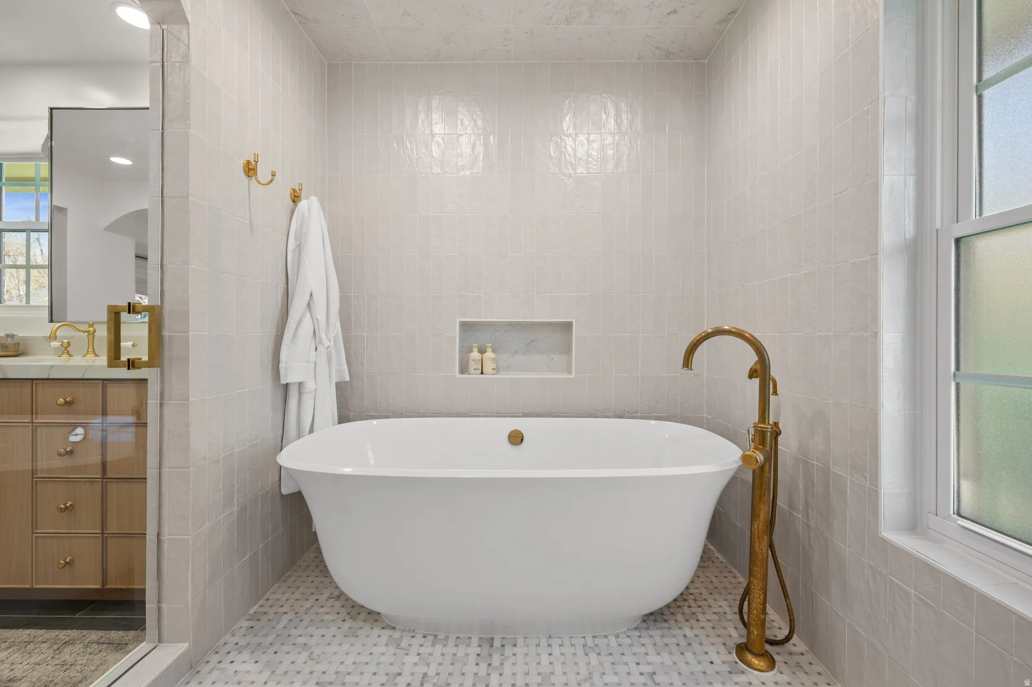 Freestanding soaking tub with a floor-mounted brass faucet, set against a tiled wall with a recessed niche
