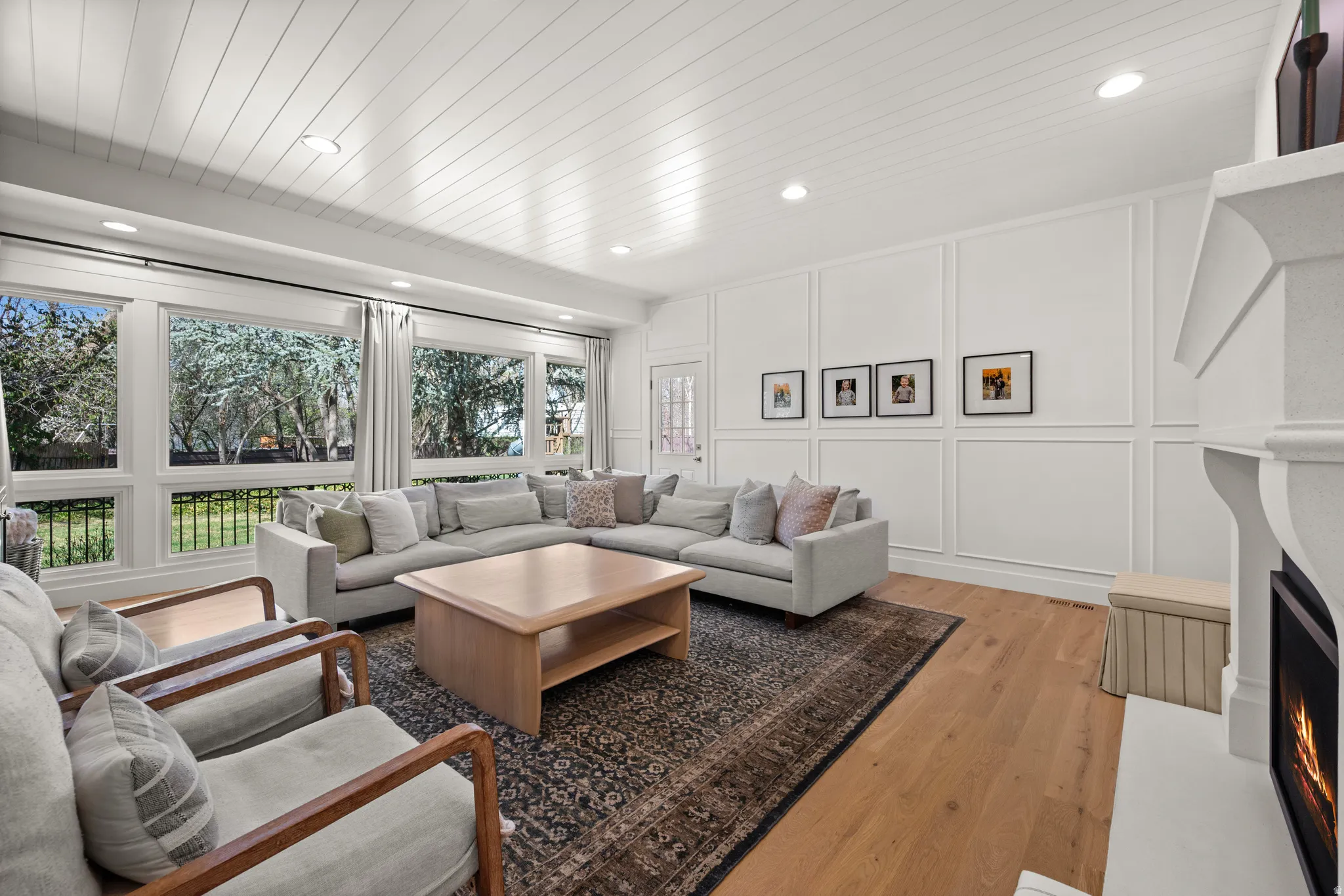 Spacious living area featuring wood-finish flooring, a detailed white panel accent wall, a built-in fireplace with a substantial mantel, and a shiplap ceiling