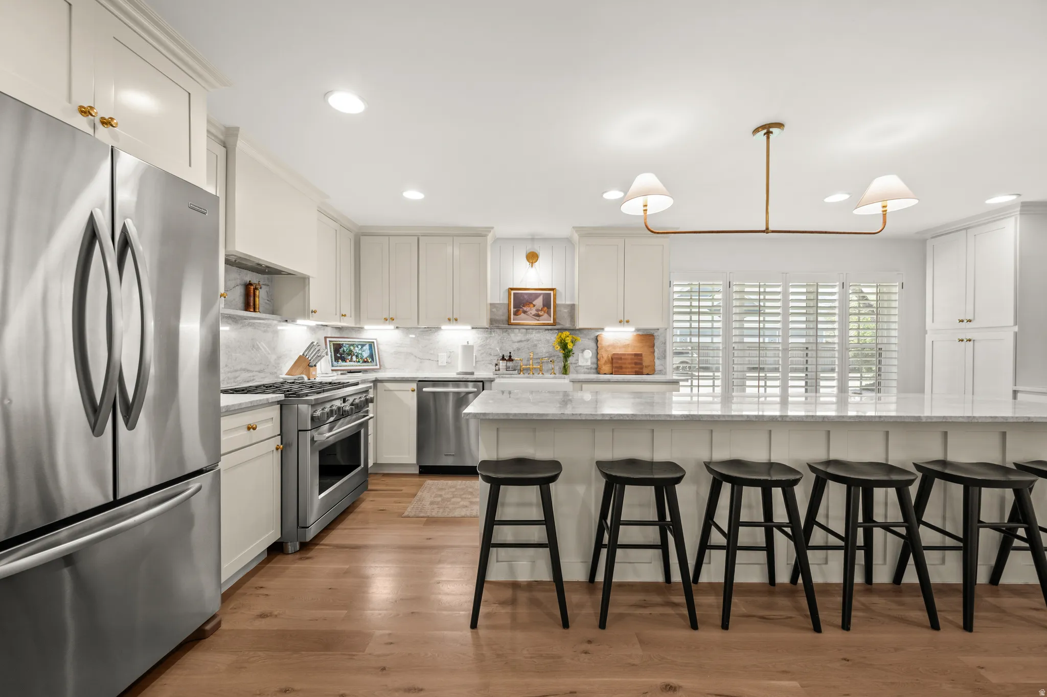 Gourmet kitchen with an expansive island featuring seating for five, stainless steel appliances, marble countertops, and light wood-finish flooring