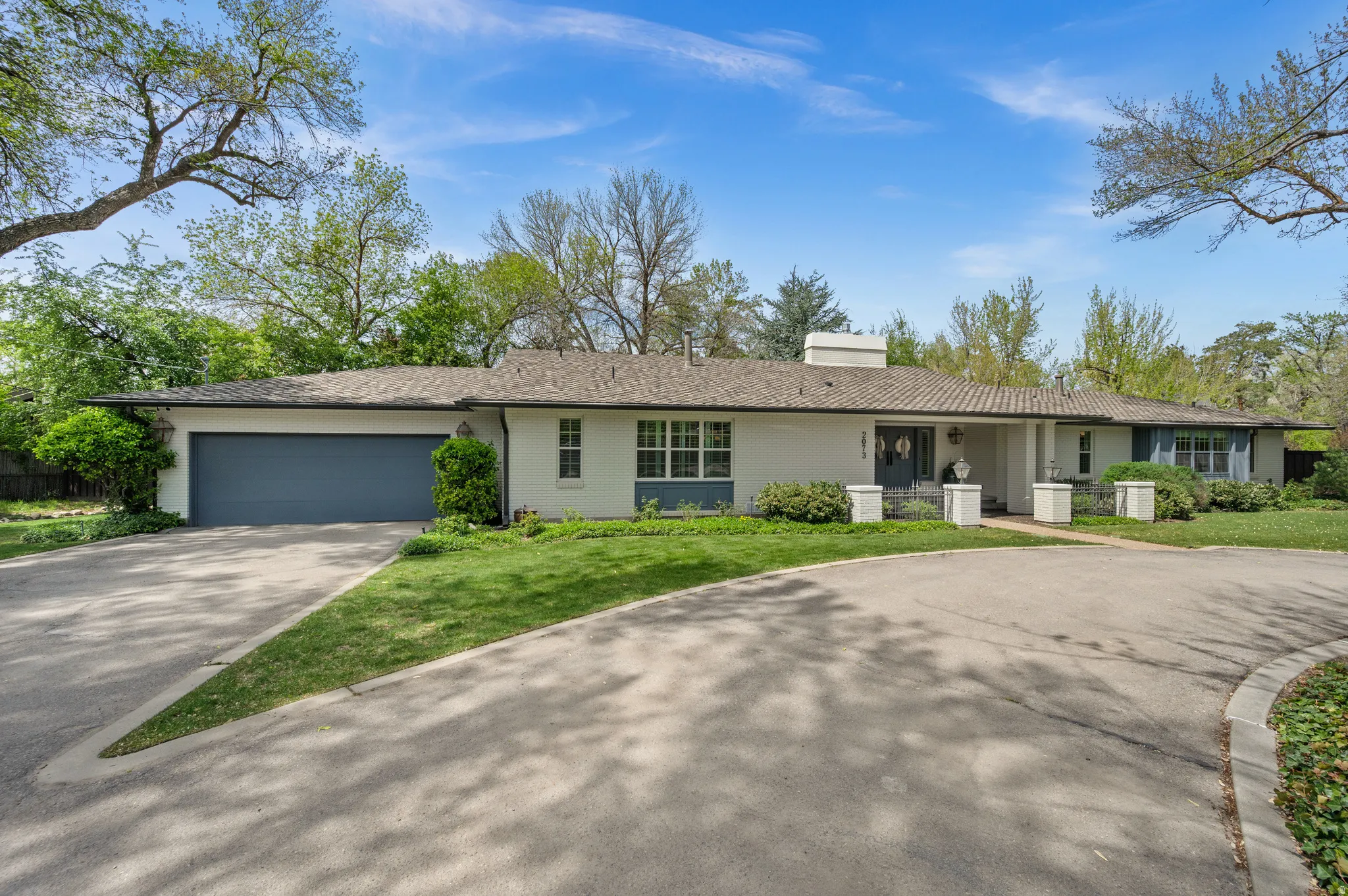 Ranch-style residence featuring a white stucco exterior, dark shingle roof, attached two-car garage with a blue door, and a circular driveway