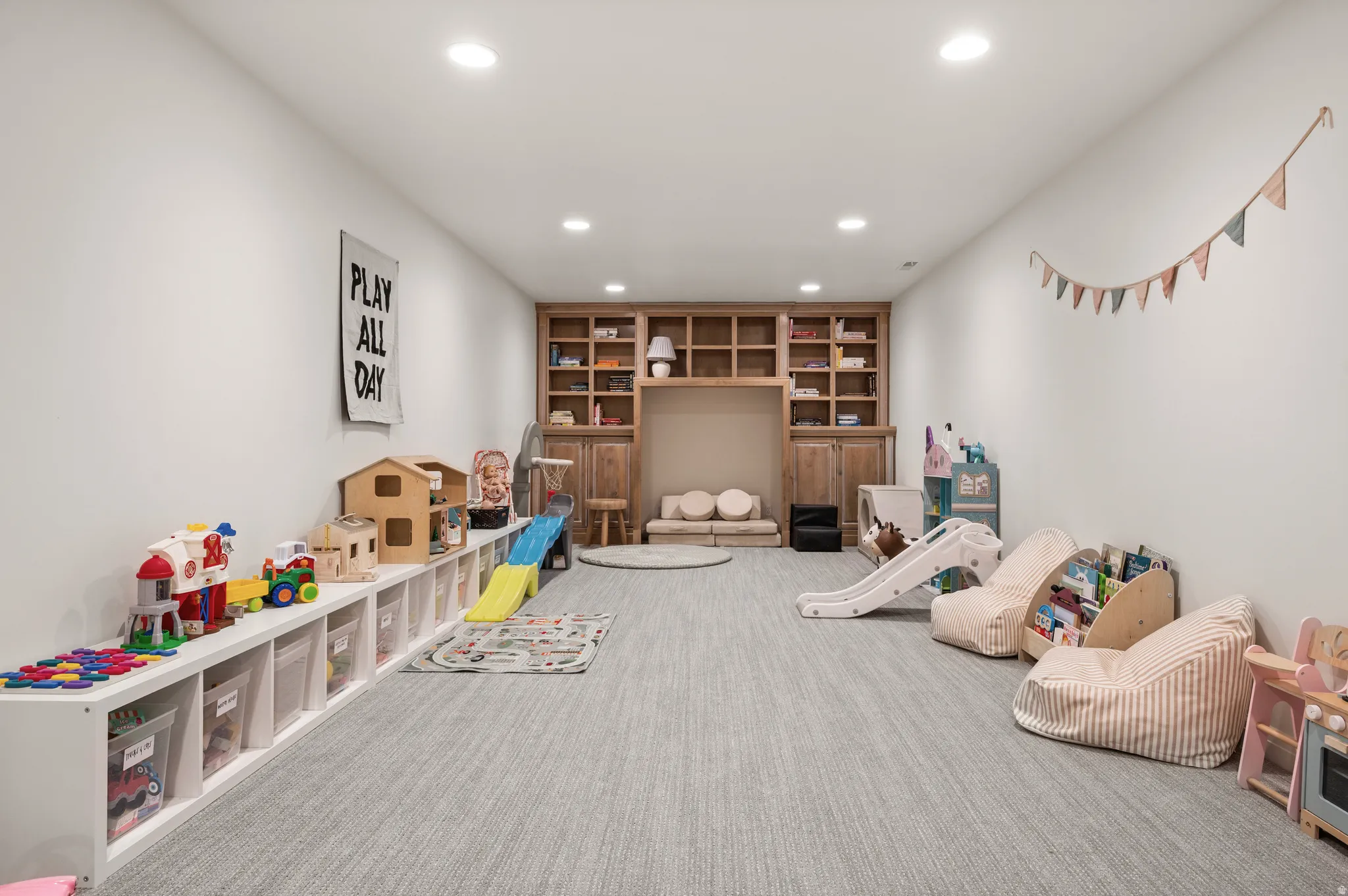 Recessed lighting illuminates a spacious room featuring a light gray carpeted floor