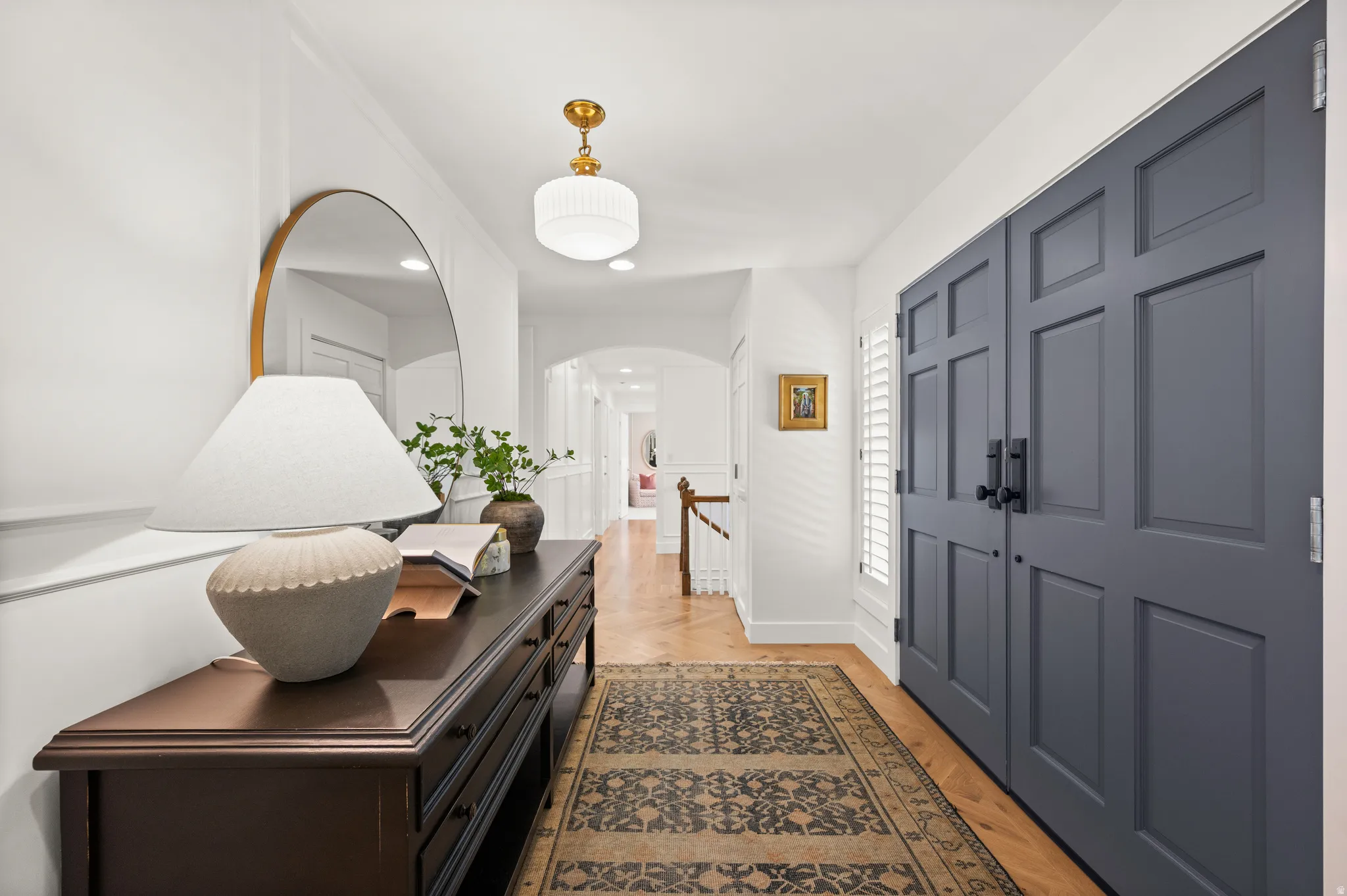 Entryway featuring hardwood flooring, a gold-toned chandelier, paneled double doors with matte black hardware, and white plantation shutters