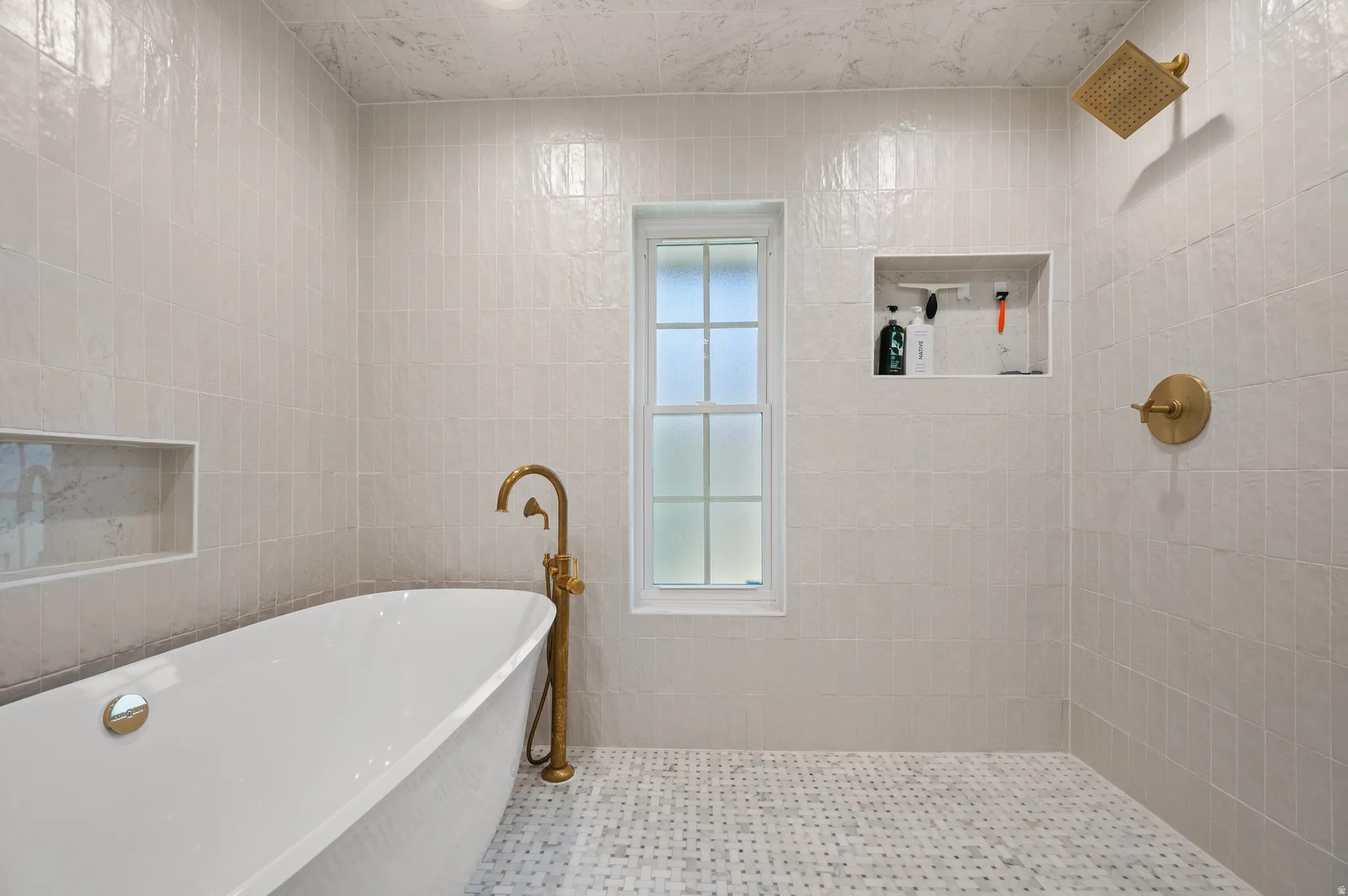 Freestanding soaking tub with a floor-mounted brass faucet, walk-in shower with brass fixtures, and mosaic floor tiling