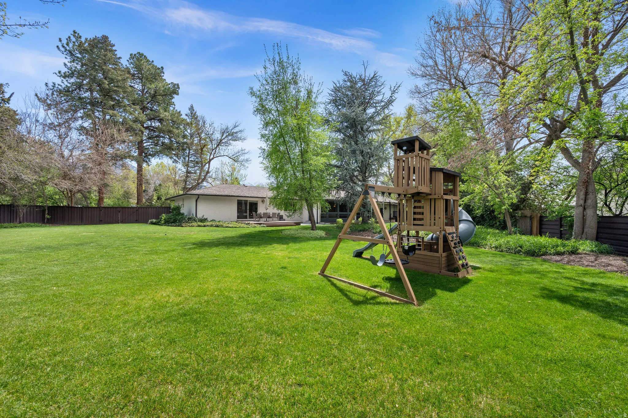 Spacious backyard featuring a manicured lawn, established trees, and a privacy fence