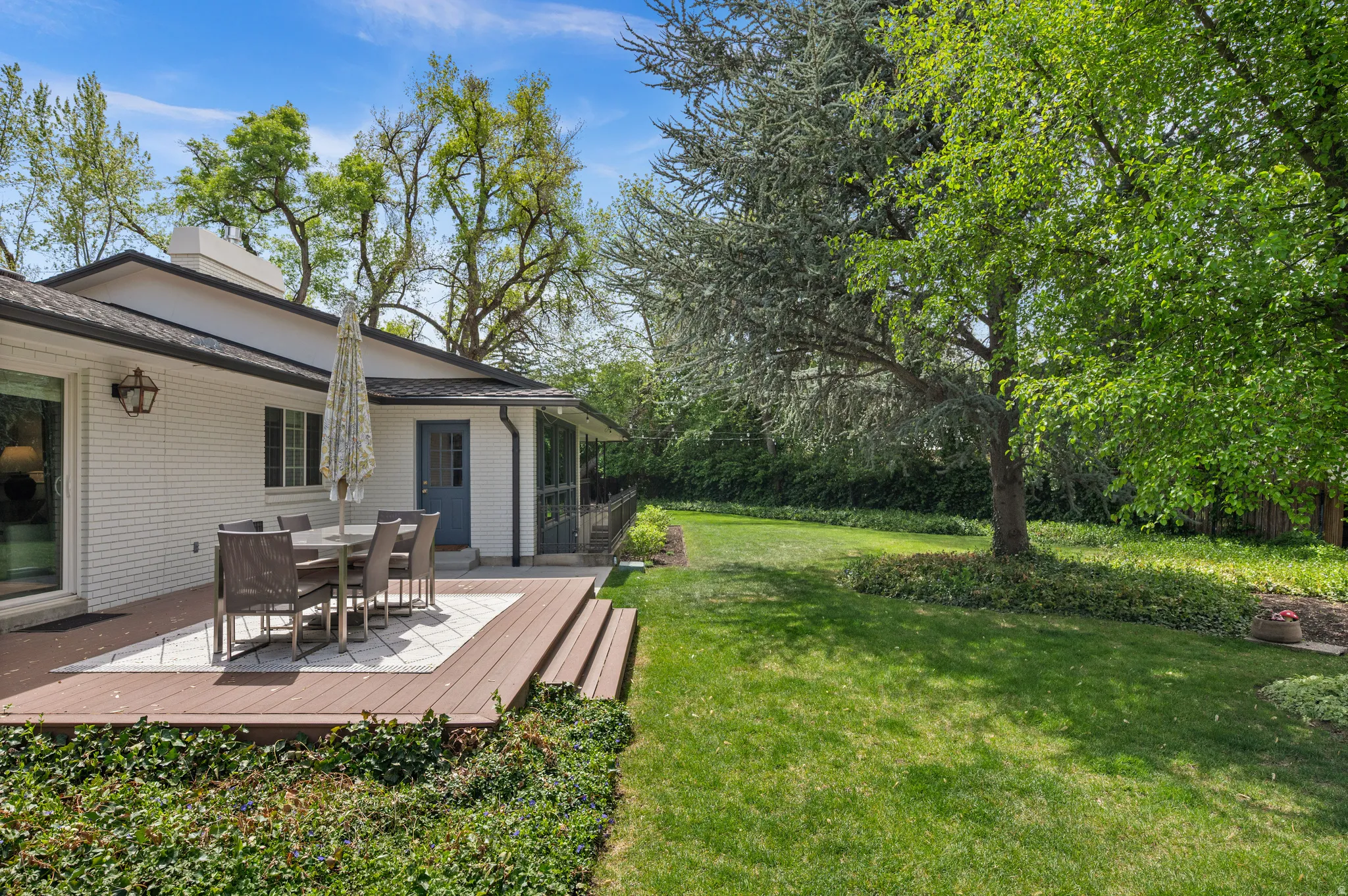 Expansive backyard featuring a multi-level composite deck with stone inlay, a manicured lawn, and mature trees