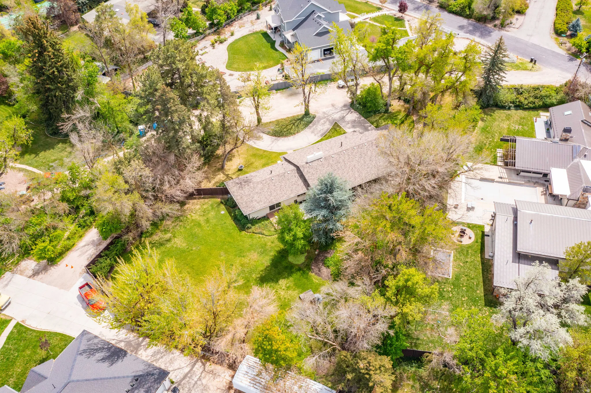 Expansive property featuring a single-story residence with a shingle roof, surrounded by mature trees and lush green lawns