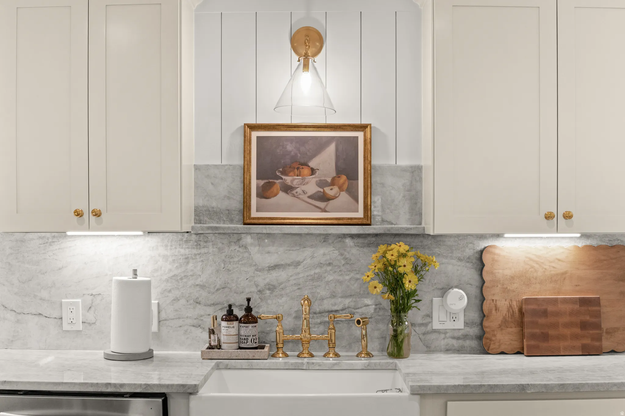 Kitchen featuring a white farmhouse sink, gold-finish faucet, stone countertops, and a stone backsplash