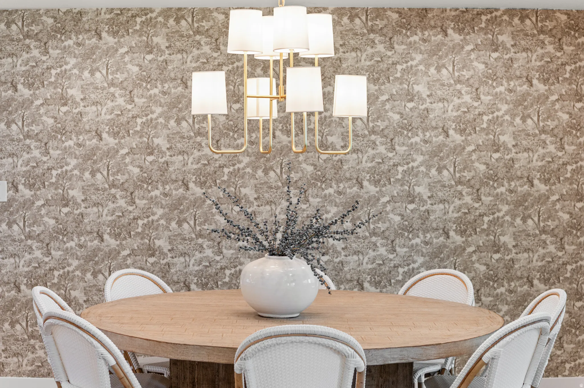 Dining area featuring an oval wood-finish table, wall-mounted light switch, and a chandelier with white drum shades