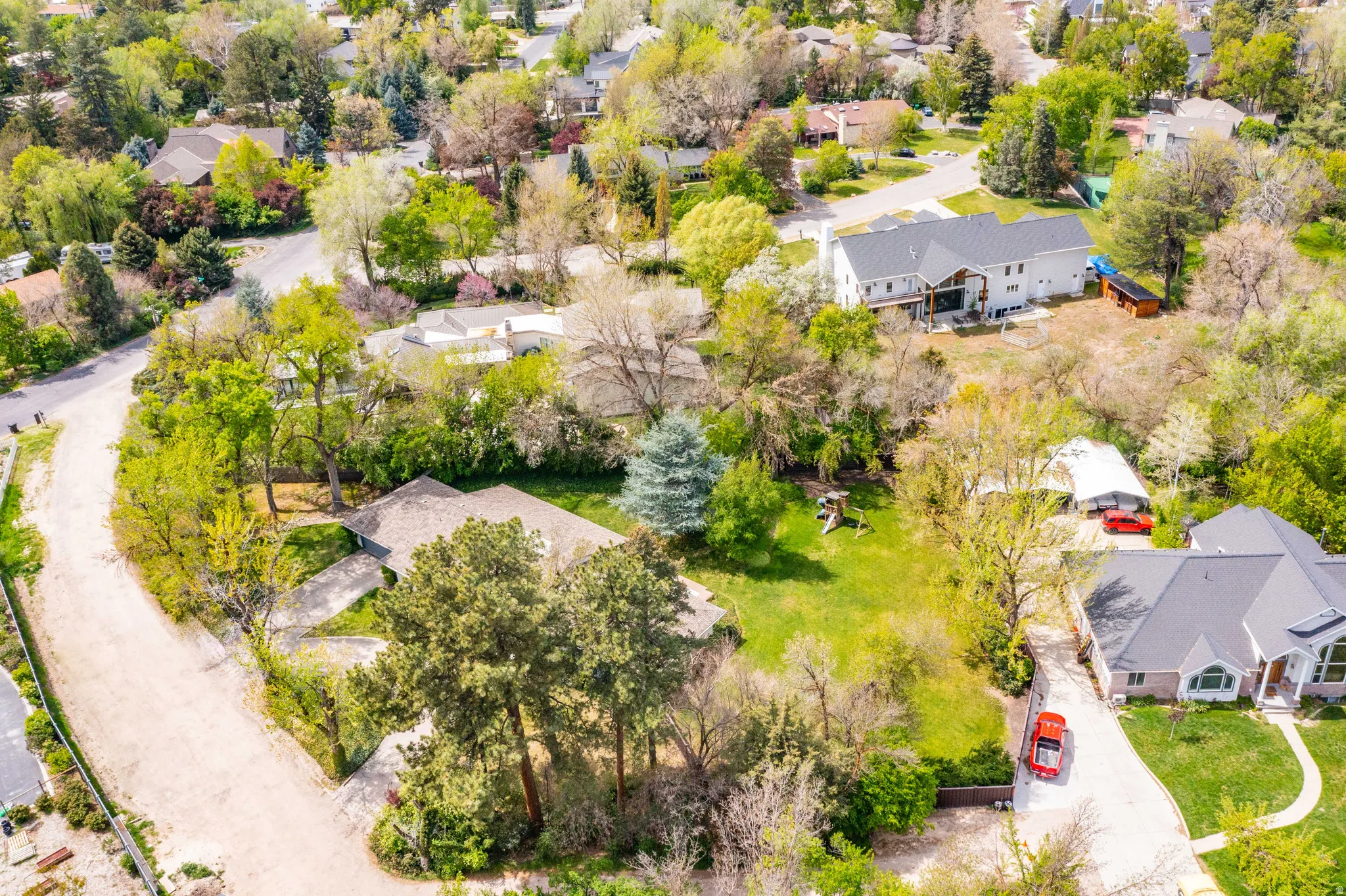 Expansive property featuring a large green space, mature trees, and a paved driveway