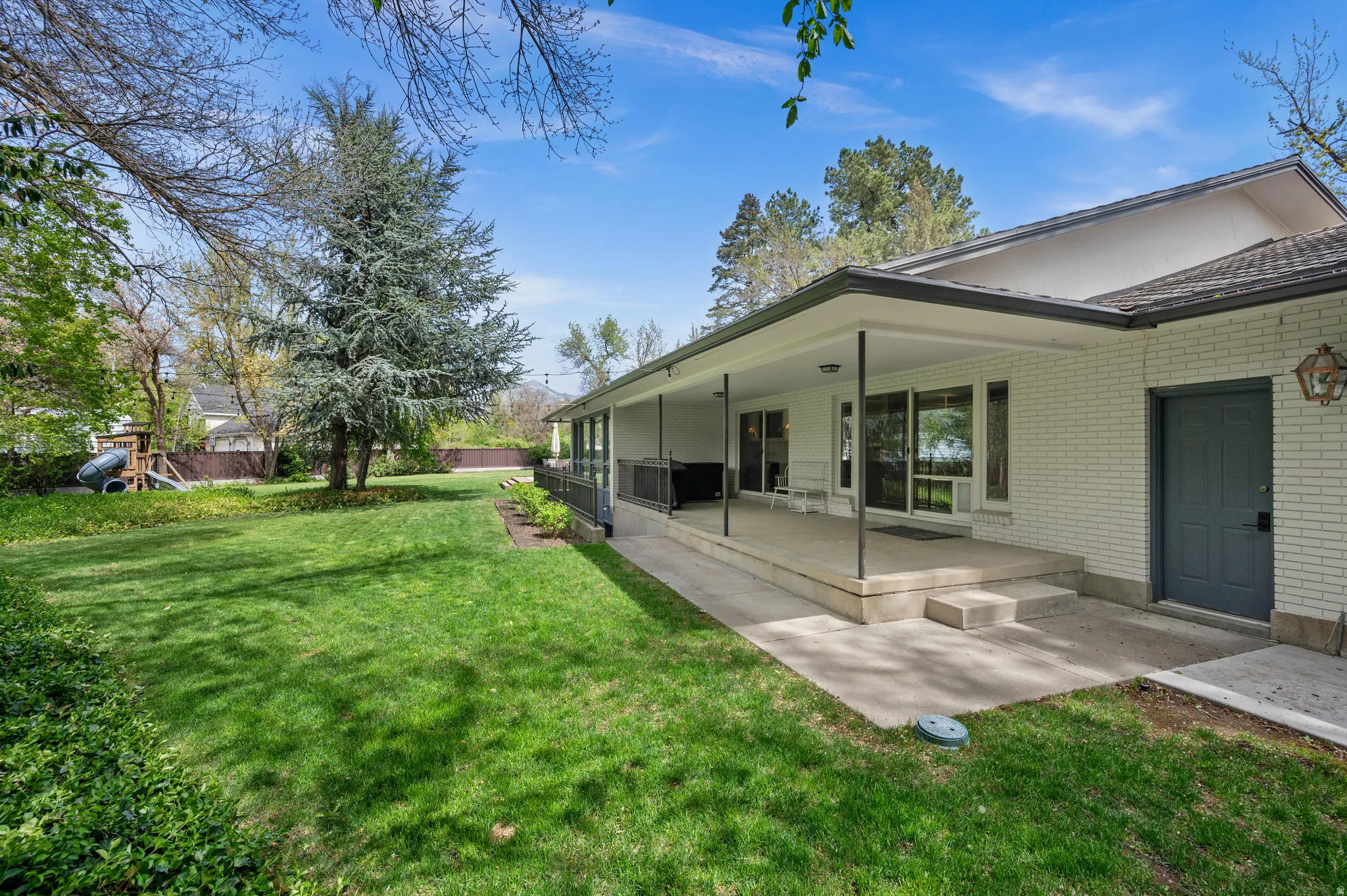 Expansive rear yard featuring a manicured lawn, mature trees, and a covered patio