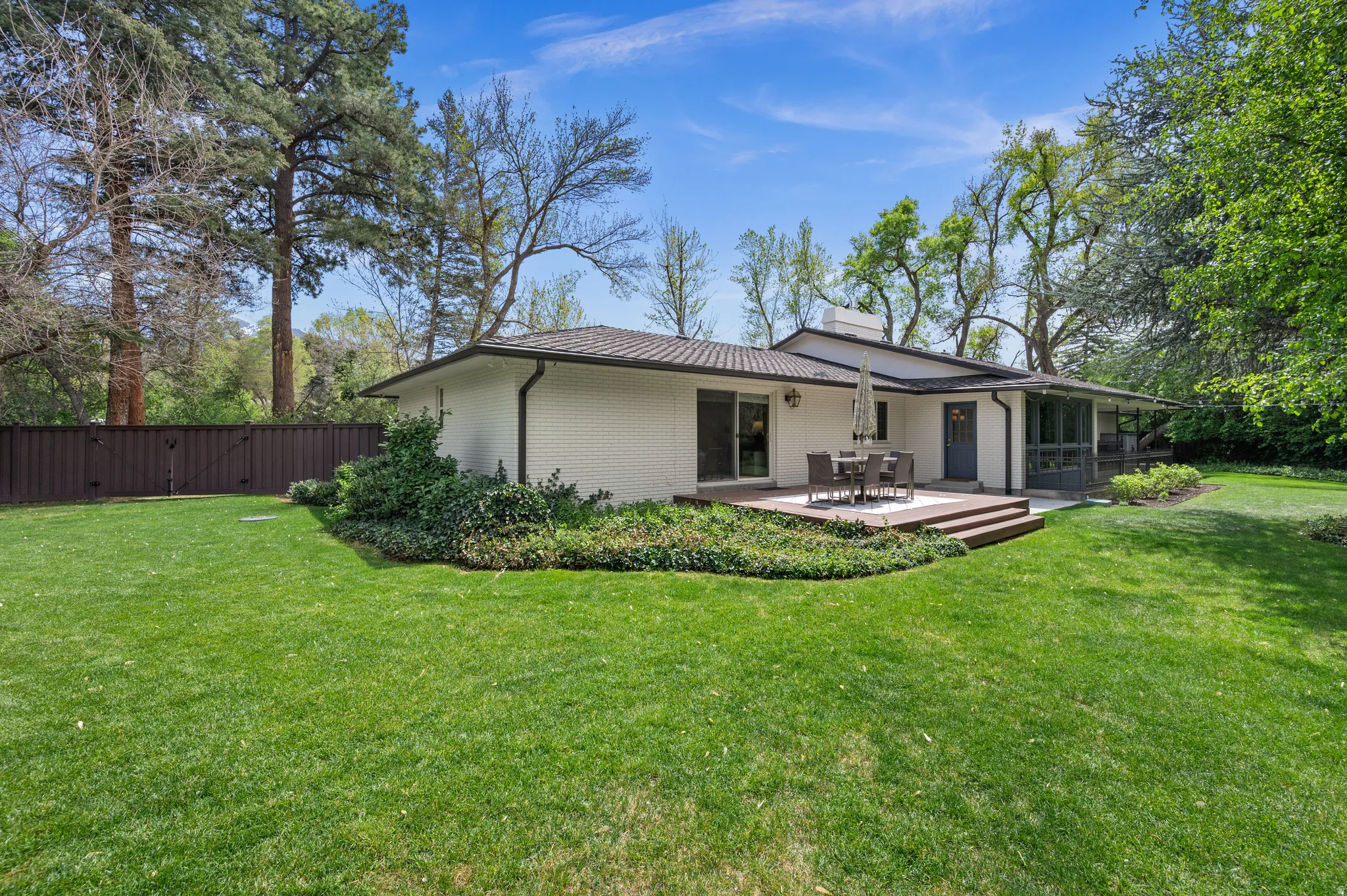 Expansive green lawn bordering a white brick residence with a tiered wood deck