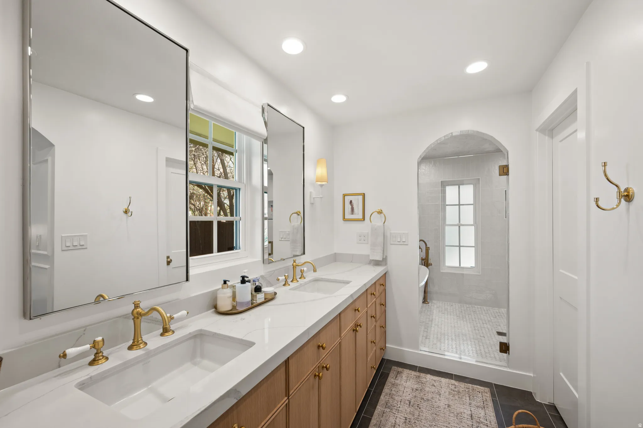 Double vanity featuring white countertops with integrated sinks, gold-finish fixtures, and natural wood cabinetry
