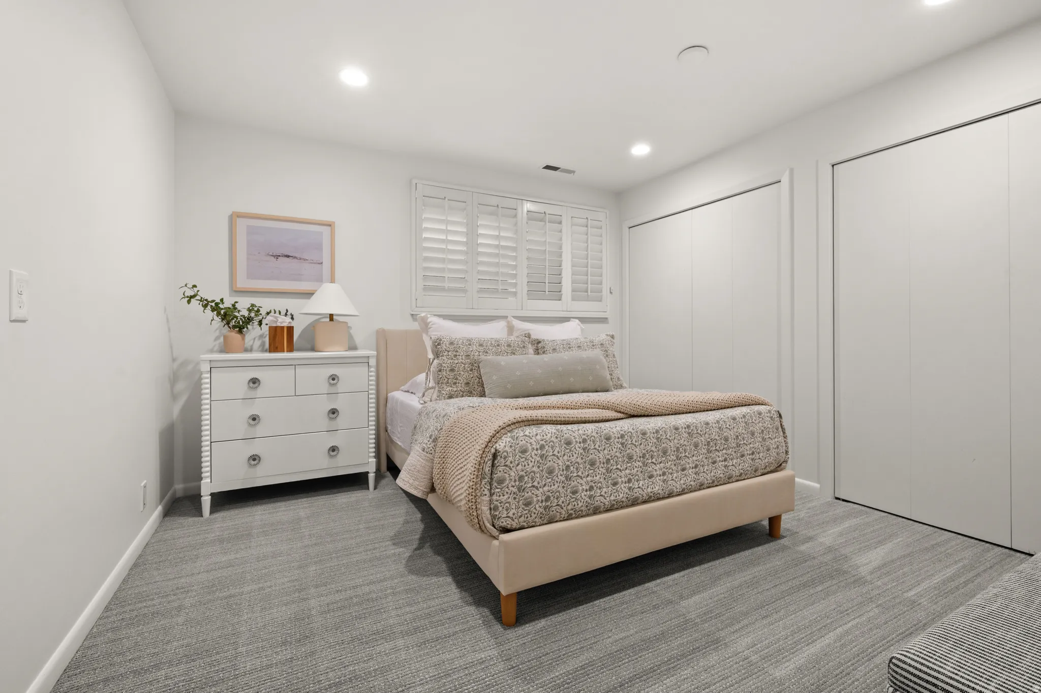 Bedroom featuring neutral wall paint, gray patterned carpet, recessed lighting, white louvered window shutters, and two integrated closet doors