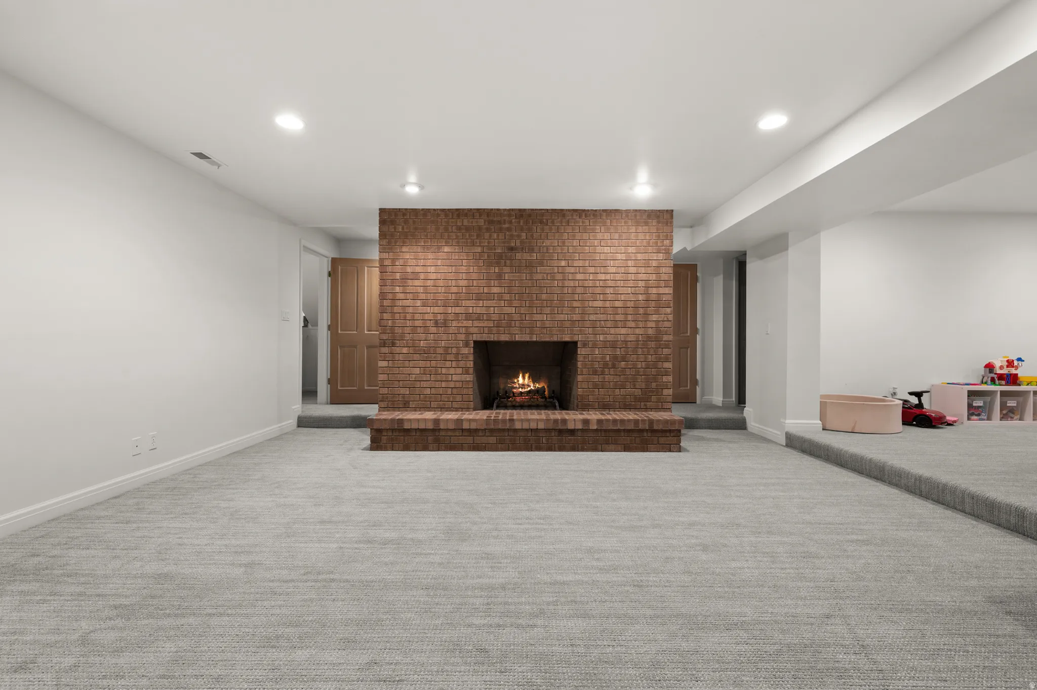 Spacious room featuring a central brick fireplace with hearth, plush carpeting, recessed lighting, and white baseboards