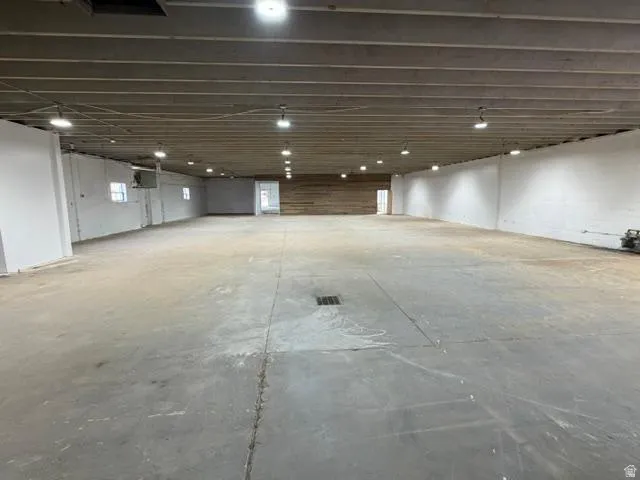 Spacious open interior featuring a concrete floor, exposed concrete ceiling with industrial lighting, white painted walls, and a wood-paneled accent wall