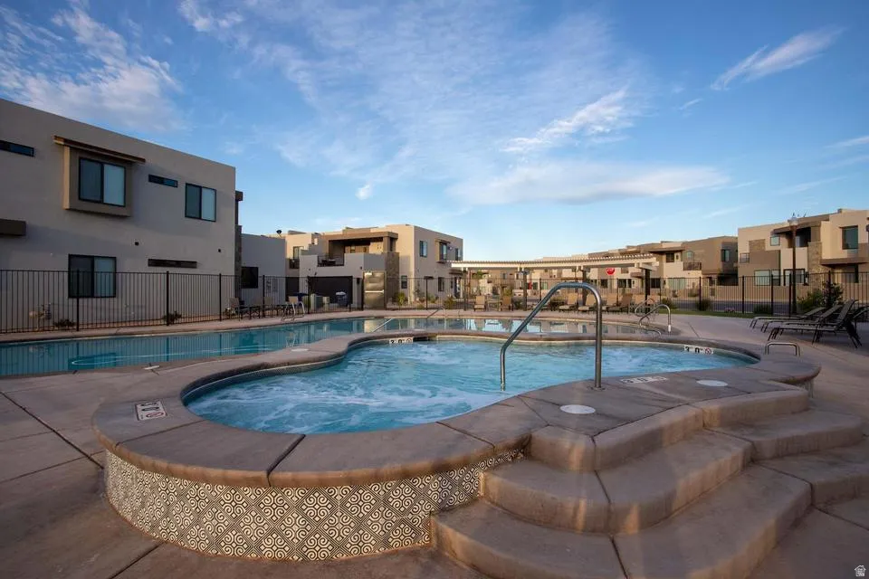 Outdoor spa with decorative tile surround and integrated steps, alongside a large swimming pool