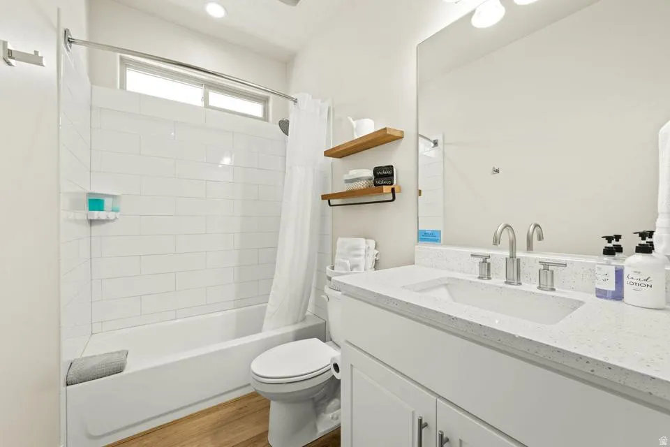 Bathroom featuring a white subway tile surround, a built-in tub, wood-finish flooring, a white vanity with a rectangular sink, and a large wall-mounted mirror