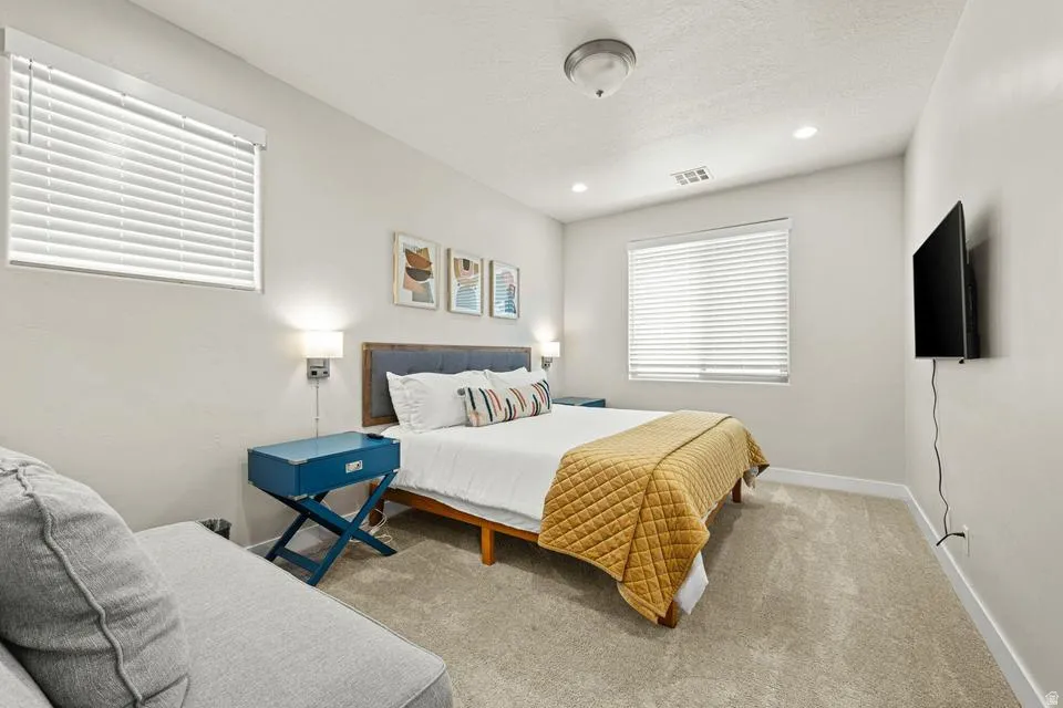 Carpeted bedroom featuring two large windows with blinds, a mounted television, a flush mount ceiling light, and recessed lighting