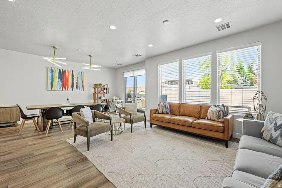 Open-concept living space featuring wood-finish flooring, recessed lighting, and multiple large windows with blinds