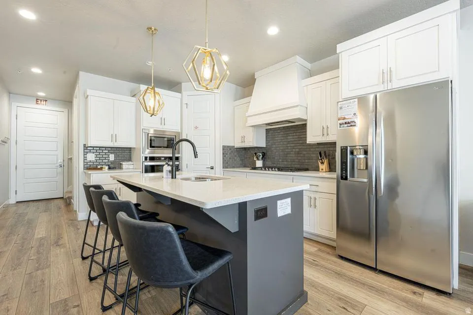 Modern kitchen featuring a central island with countertop seating, stainless steel appliances, a tile backsplash, light-toned cabinetry, and wood-finish flooring