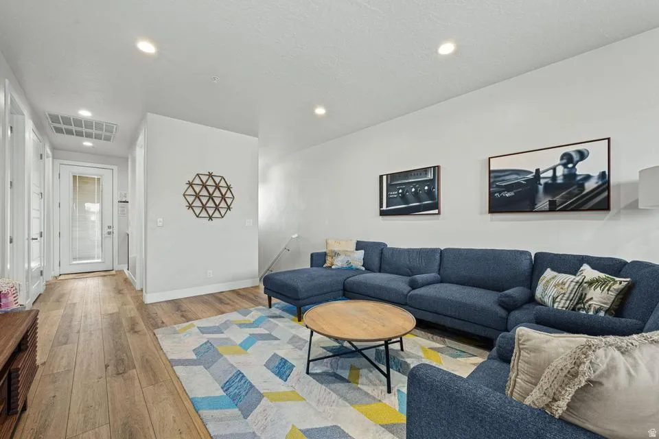 Open-concept living area with wood-finish flooring, recessed lighting, and a white interior door with frosted glass