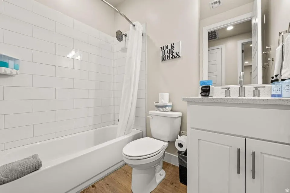 Bathroom featuring a white subway tile shower surround, a built-in bathtub, wood-finish flooring, a white vanity with cabinet storage, and a light-colored countertop