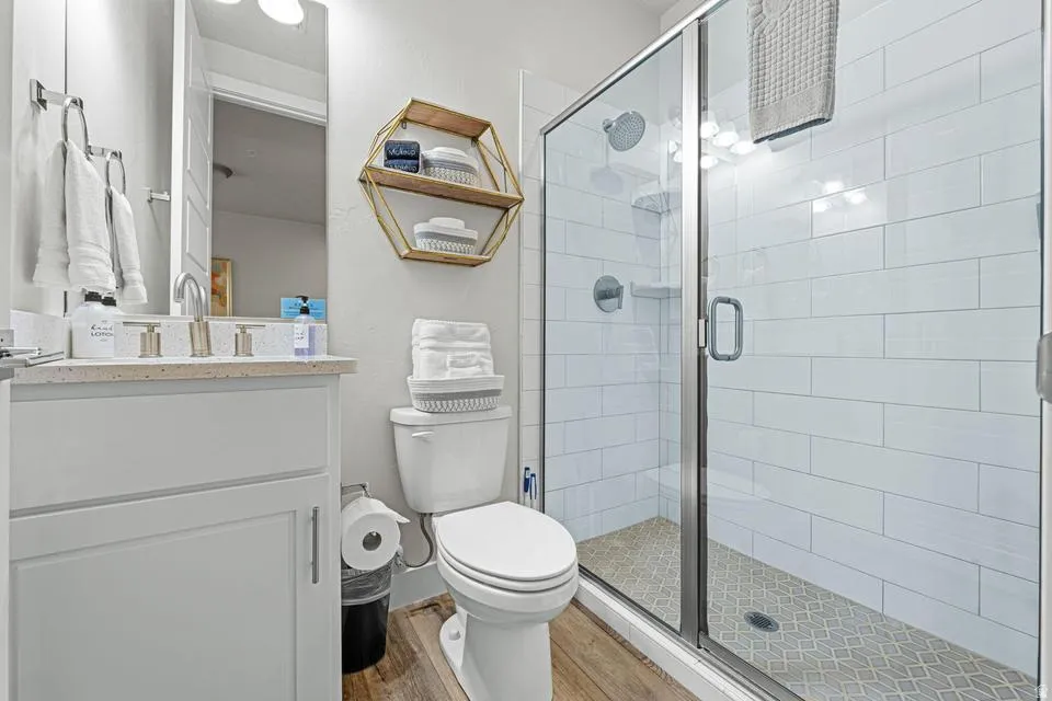 Bathroom featuring a glass-enclosed shower with white subway tile, a vanity with a light-colored countertop, and wood-finish flooring
