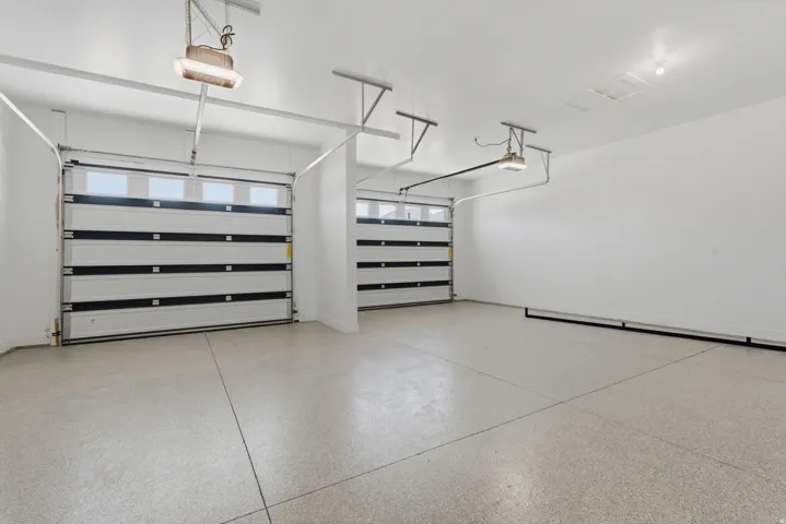 Bright white garage interior featuring two garage doors with window panels and a speckled epoxy floor finish